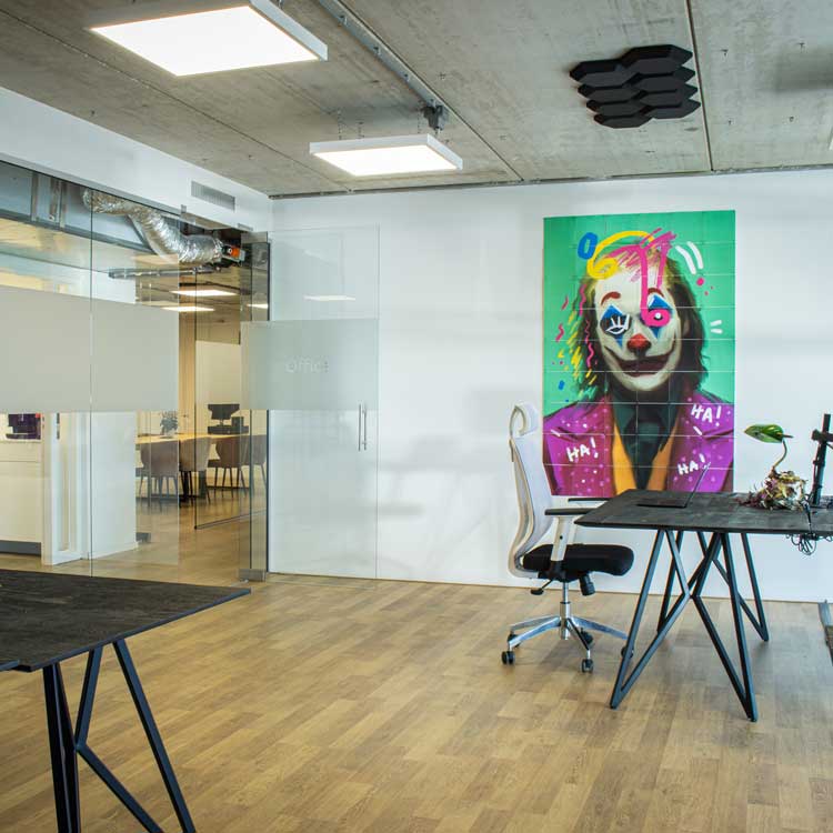 Modern office space with wooden floor, glass walls, black tables, white office chair, and colorful Joker-themed graffiti on the wall of Onesix